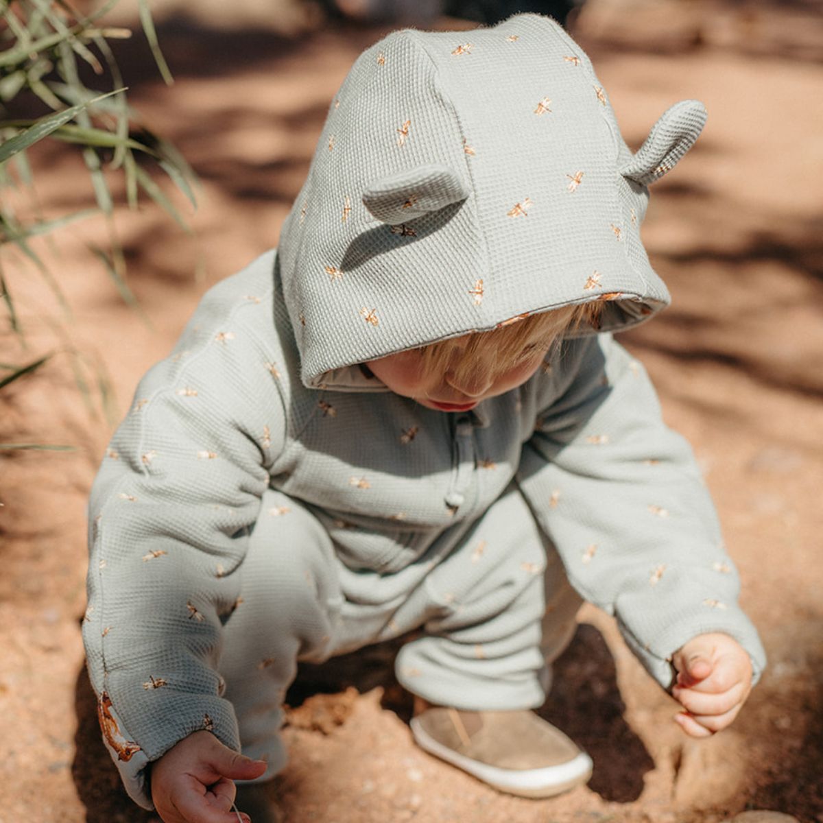 A toddler or baby kneeling down in the dir wearing the Fox and Dragonfly Reversible Waffle Knit Quilted Hooded Jumpsuit with a focus on the animal ears