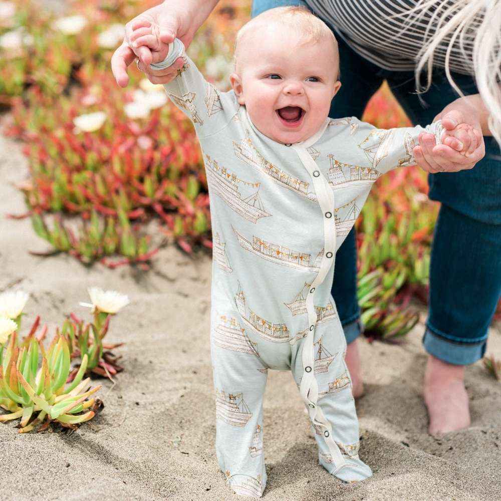 Little Boy on the Beach Wearing Blue Ships Bamboo Footed Romper by Milkbarn Kids