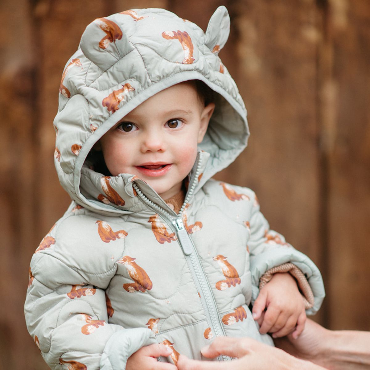 Toddler looking at the camera wearing the Fox Lightweight Quilted Down Hooded Jacket with animal ears and with the hood up.