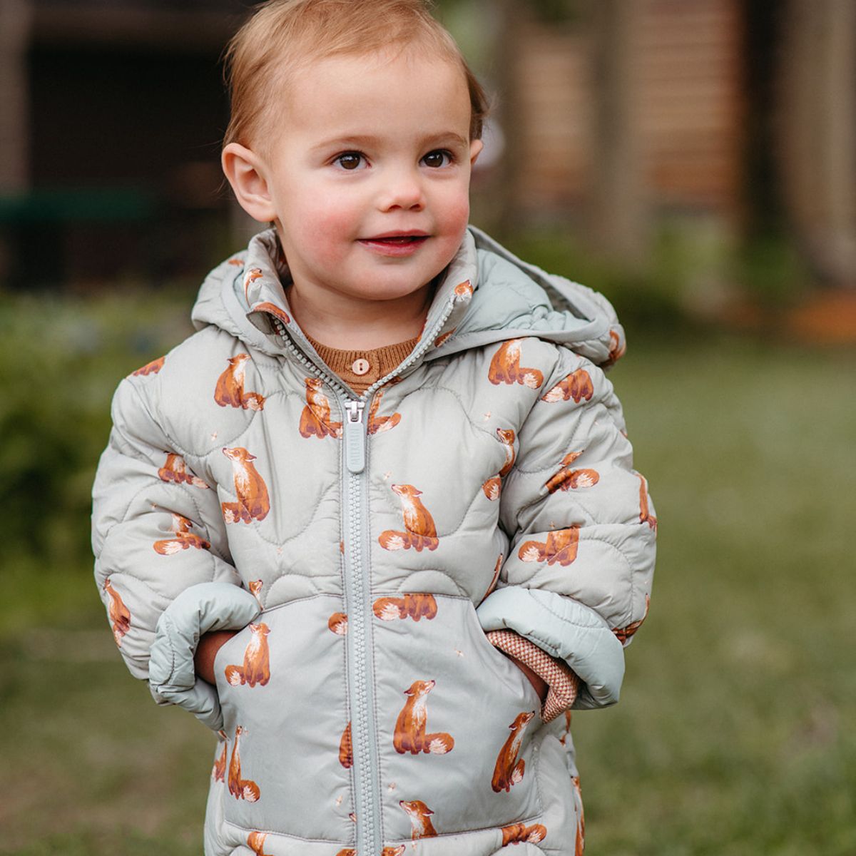 Toddler smiling with his hands in the pocket of the Fox Lightweight Quilted Down Hooded Jacket