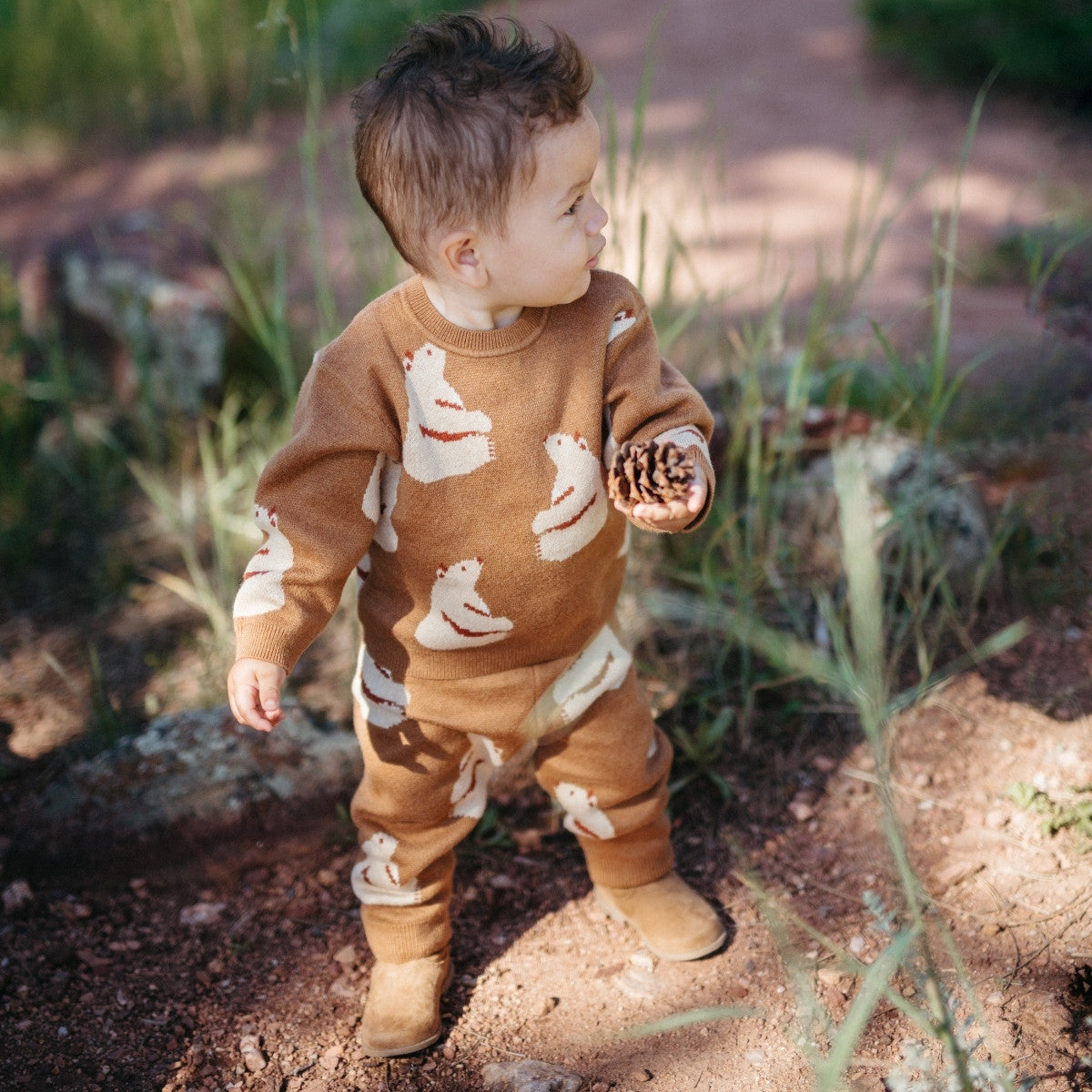 Baby boy outside holding a pinecone in the forest and wearing the Honey Bear Knitted Birdseye Jacquard Sweatpants