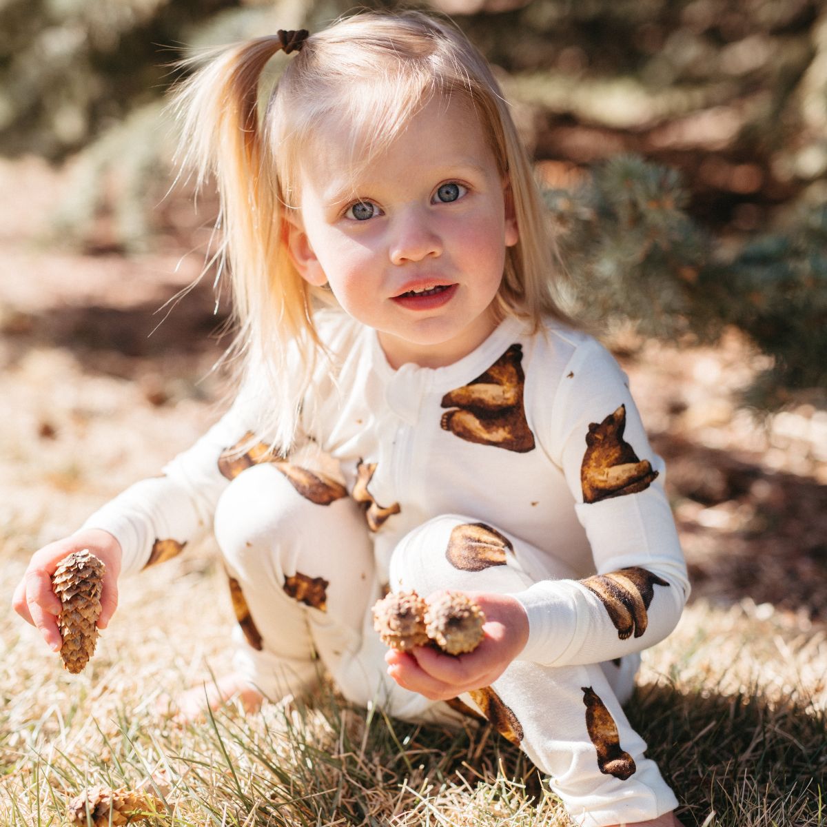 Baby girl in a park holding pinecones wearing the bamboo Honey Bear Zipper Pajama