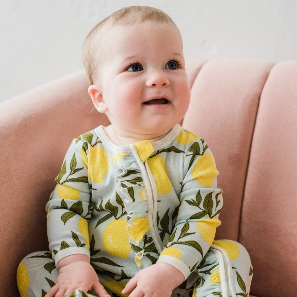Baby sitting on a pink couch wearing the Lemon Organic Cotton Ruffle Zipper Footed Romper by Milkbarn Kids
