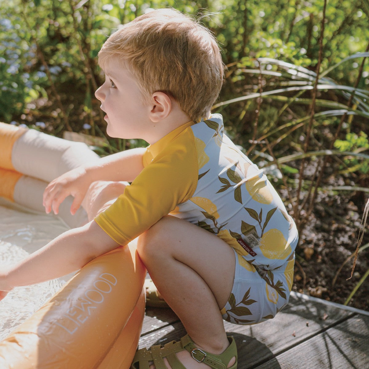 Toddler boy playing in a blow up pool wearing the Lemon Zipper Top and Swim Trunks Lifestyle 1