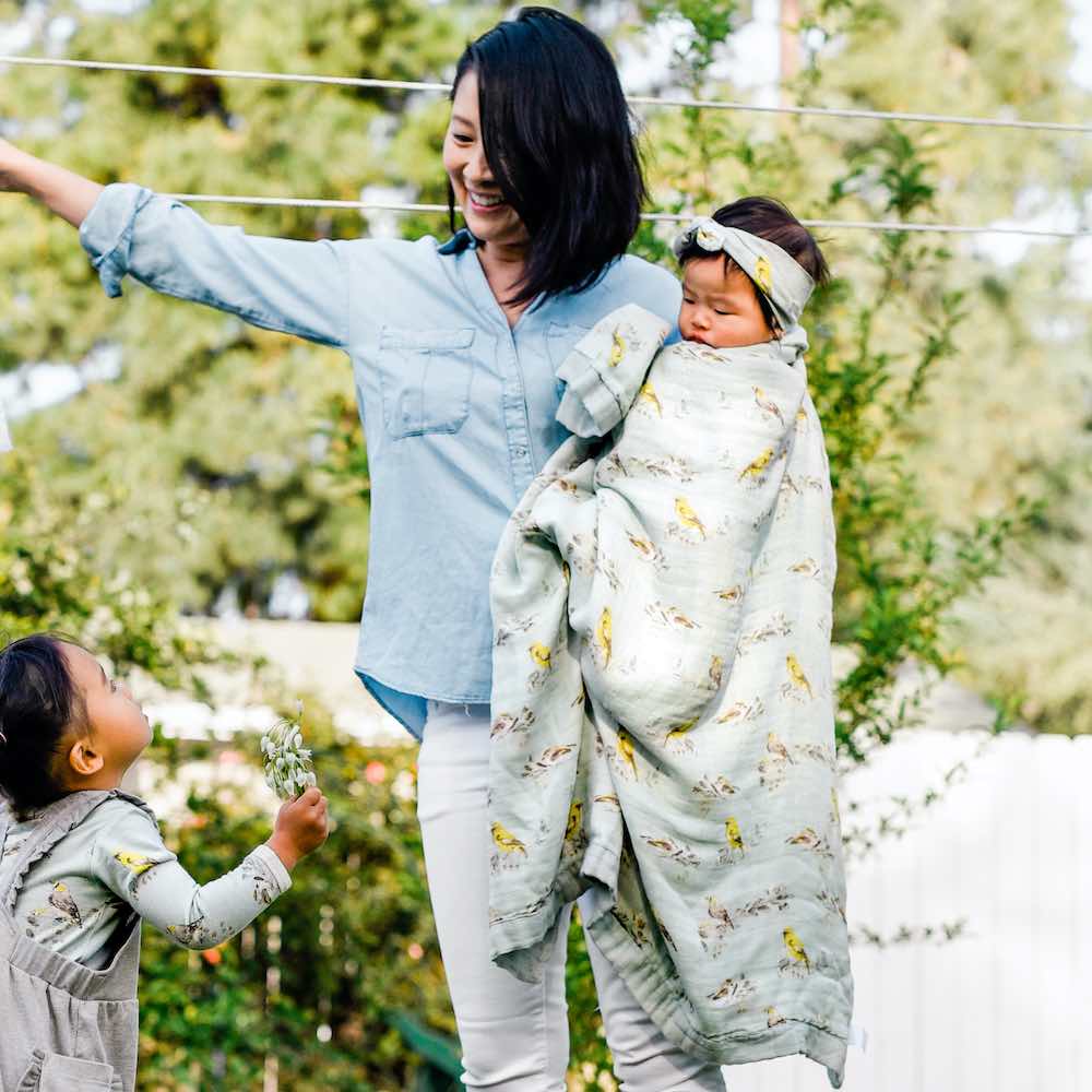 Mom holding baby girl wrapped in Milkbarn's Blue Bird print Big Lovey Blanket outside