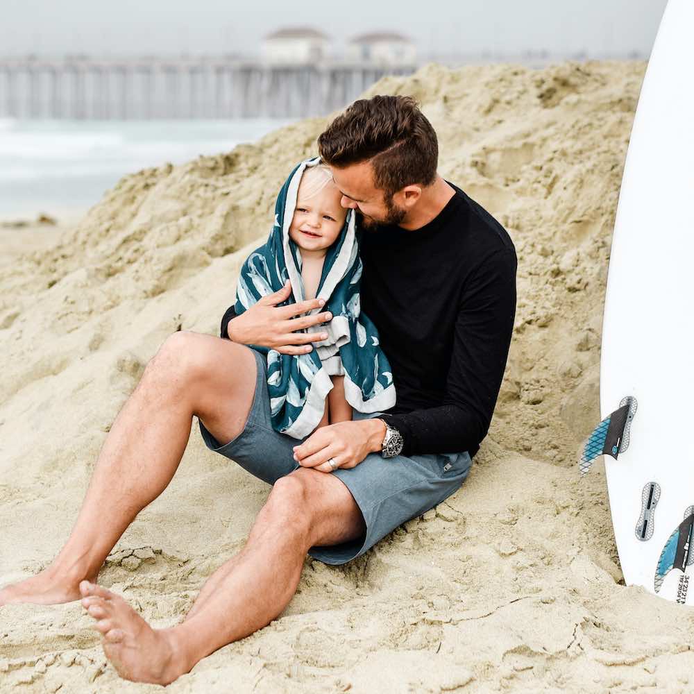 Dad and son on the beach wrapped in Milkbarn Kids Big Lovey in Blue Whale Print