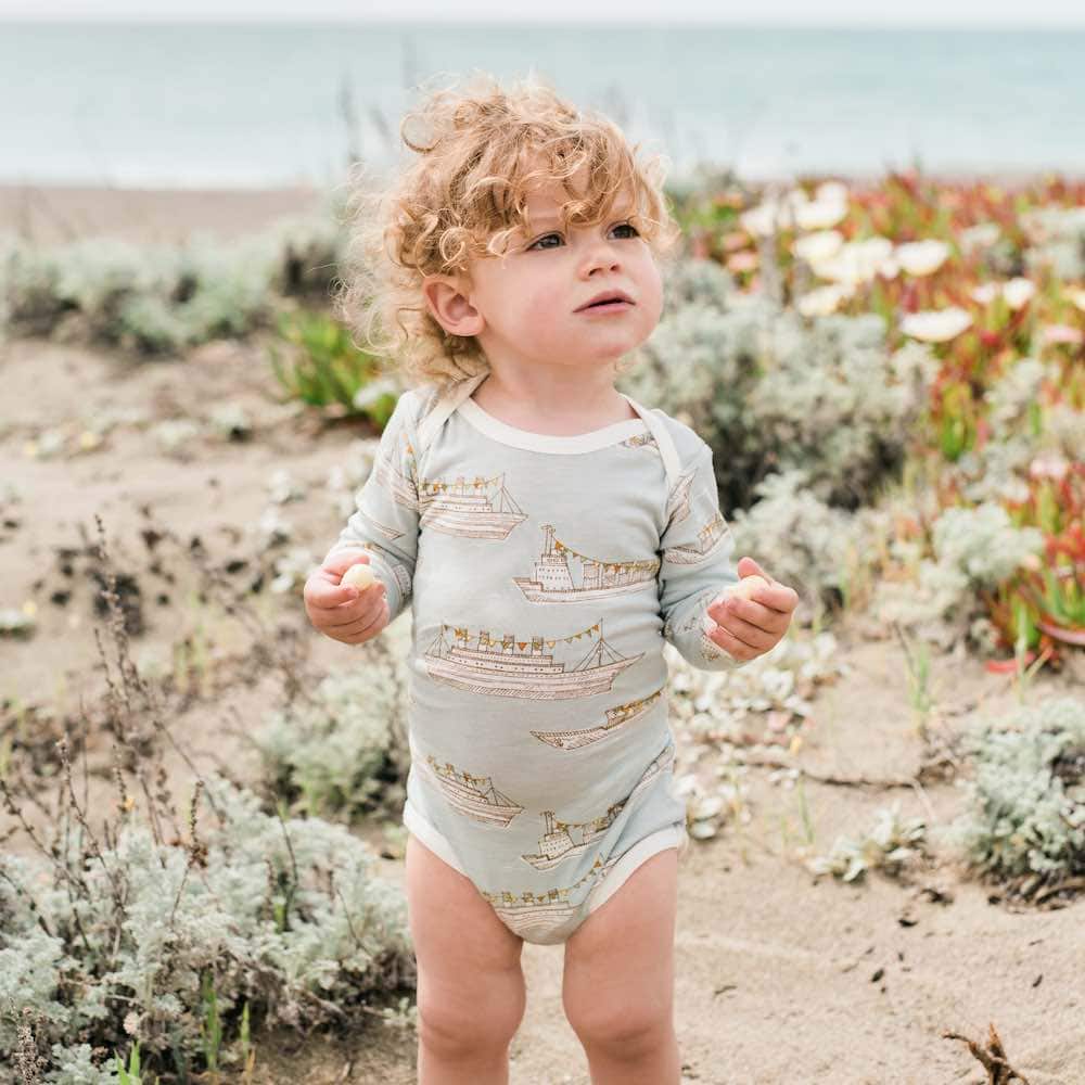 Little boy on the beach in Milkbarn Kids Long Sleeve One Piece in Bamboo Blue Ships Print