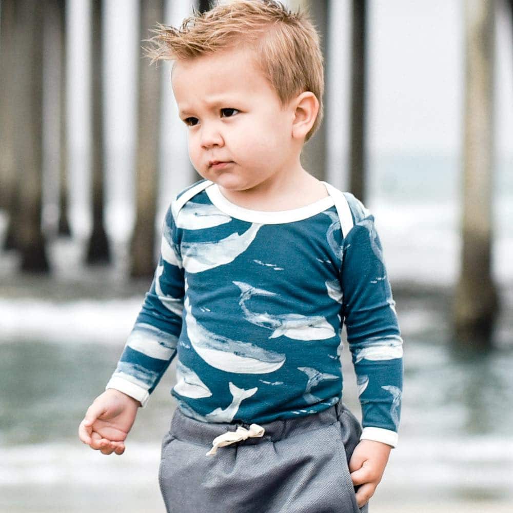 Little boy near a beach pier in Milkbarn Kids Bamboo Long Sleeve One Piece in Bamboo Blue Whale Print
