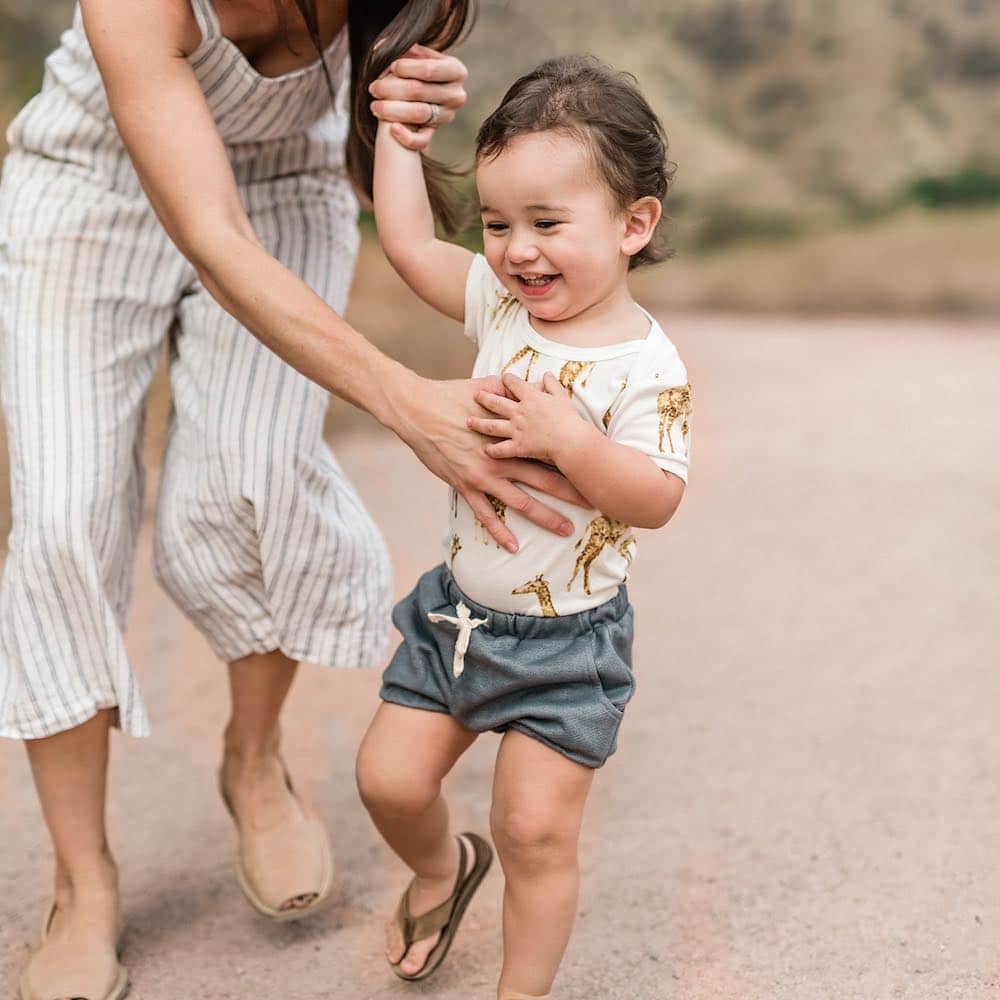 Mom and Baby Boy Wearing the Denim Pocket Bloomer and the Bamboo One Piece in the Orange Giraffe Print by Milkbarn Kids