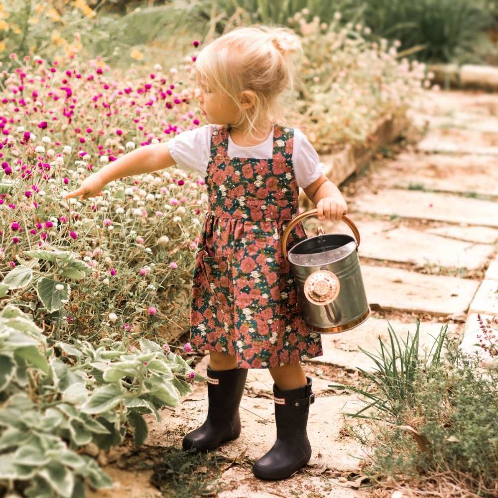 Little girl in a garden pointing to flowers wearing a Organic Pinafore Apron by Milkbarn Kids