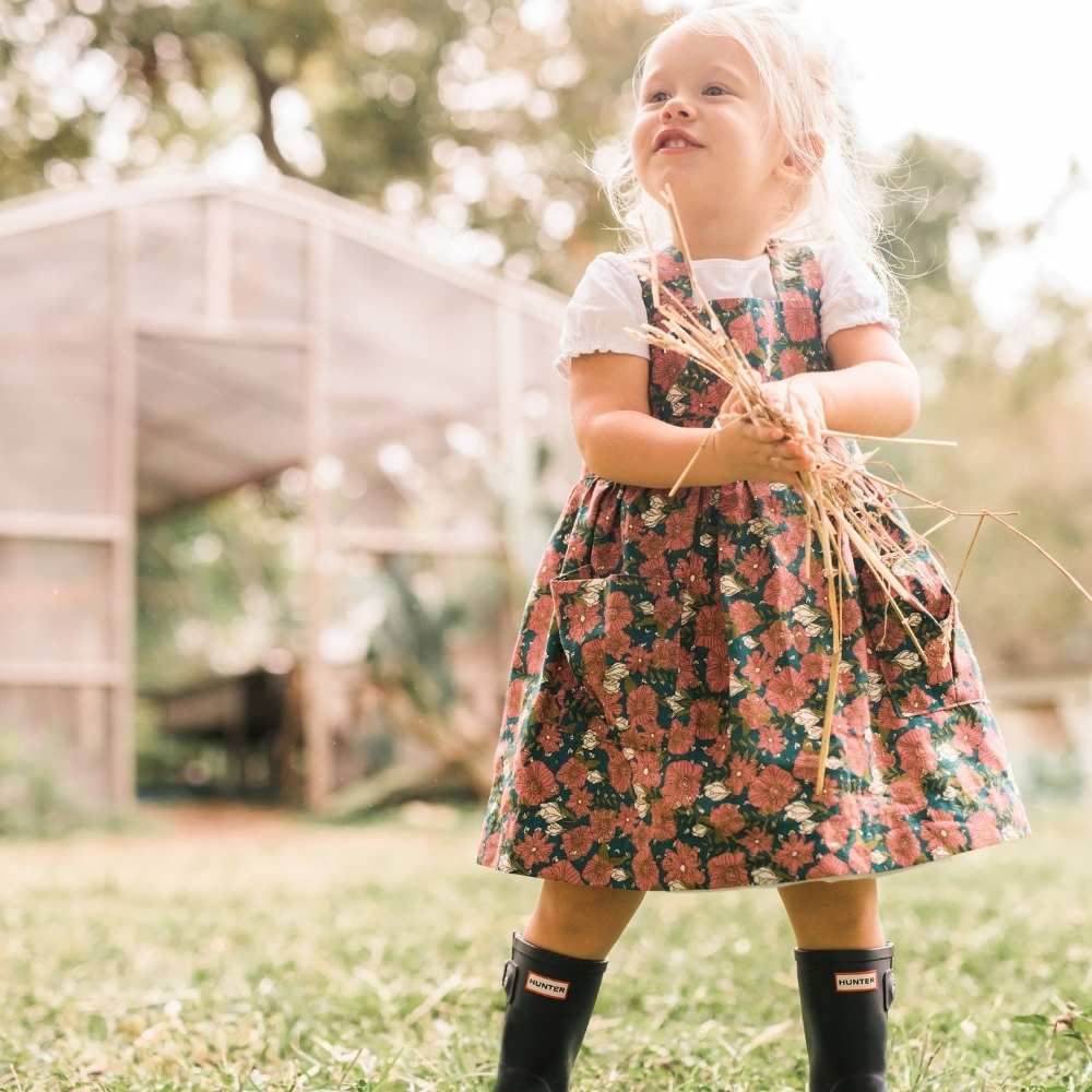 Little Girl in a garden holding hay wearing a Organic Pinafore Apron by Milkbarn Kids