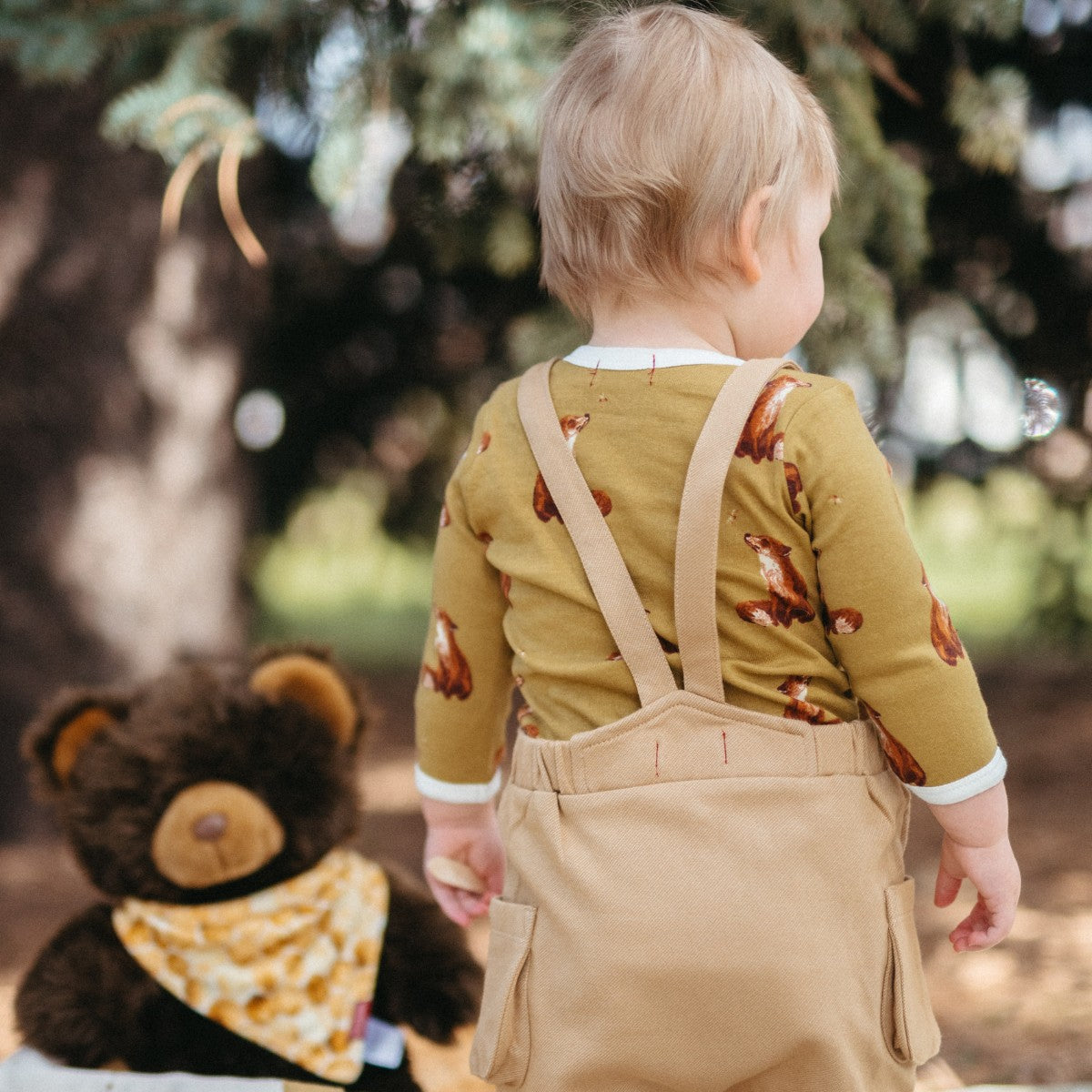 Little Boy facing away at a picnic wearing the Rust Denim Overalls and Gold Fox Long Sleeve One Piece by Milkbarn