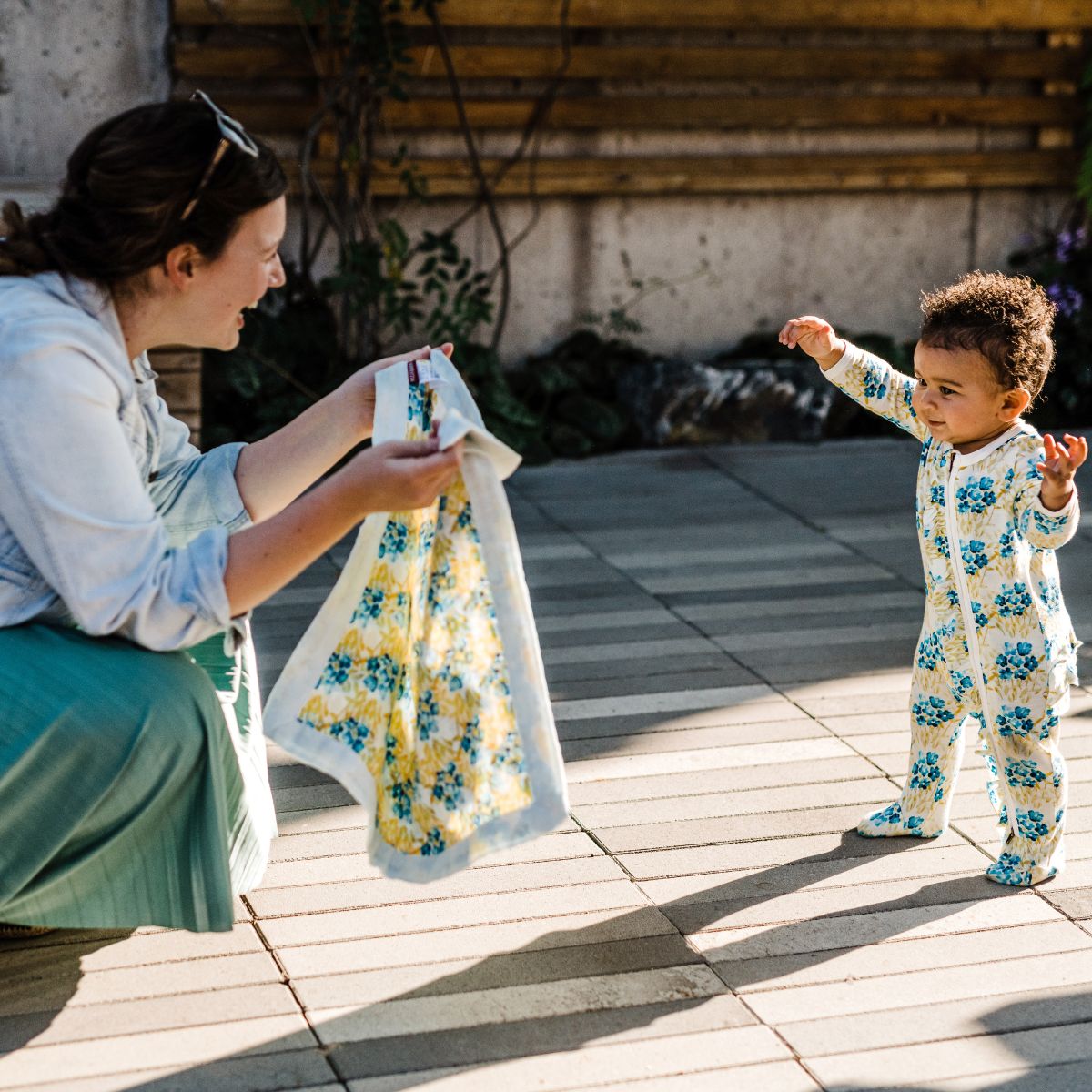 Little girl wearing matching outfit walking toward her mom holding Milkbarn Sky Floral Mini Lovey muslin security blanket