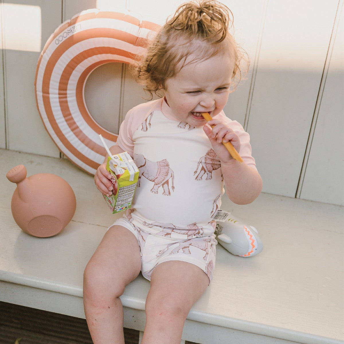 Toddler girl playing on a bench near the pool wearing the Tutu Elephant Zipper Top and Swim Trunks