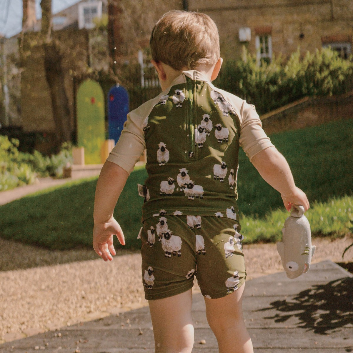 Toddler Boy walking on a path wearing the Valais Sheep Zipper Top and Swim Trunks