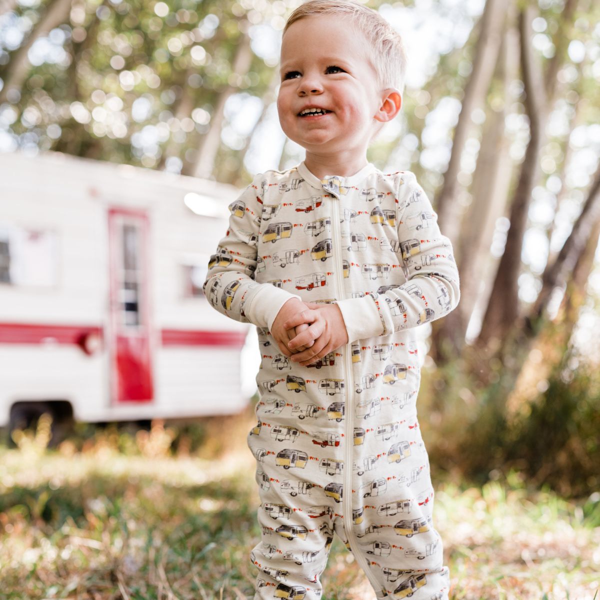 Baby Boy outside near a red and white vintage trailer wearing the organic zipper pajamas with the vintage trailers print by Milkbarn Kids