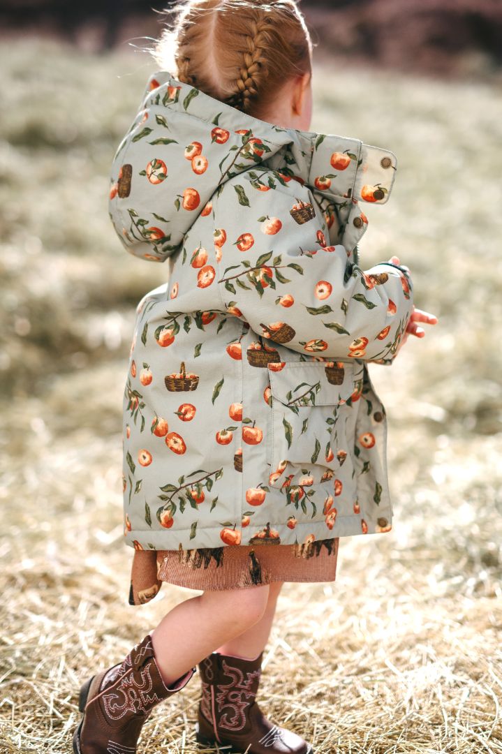 Young girl modeling Apple Orchard print nylon three-in-one autumn winter jacket, side view showing hood, front right pockets, and back