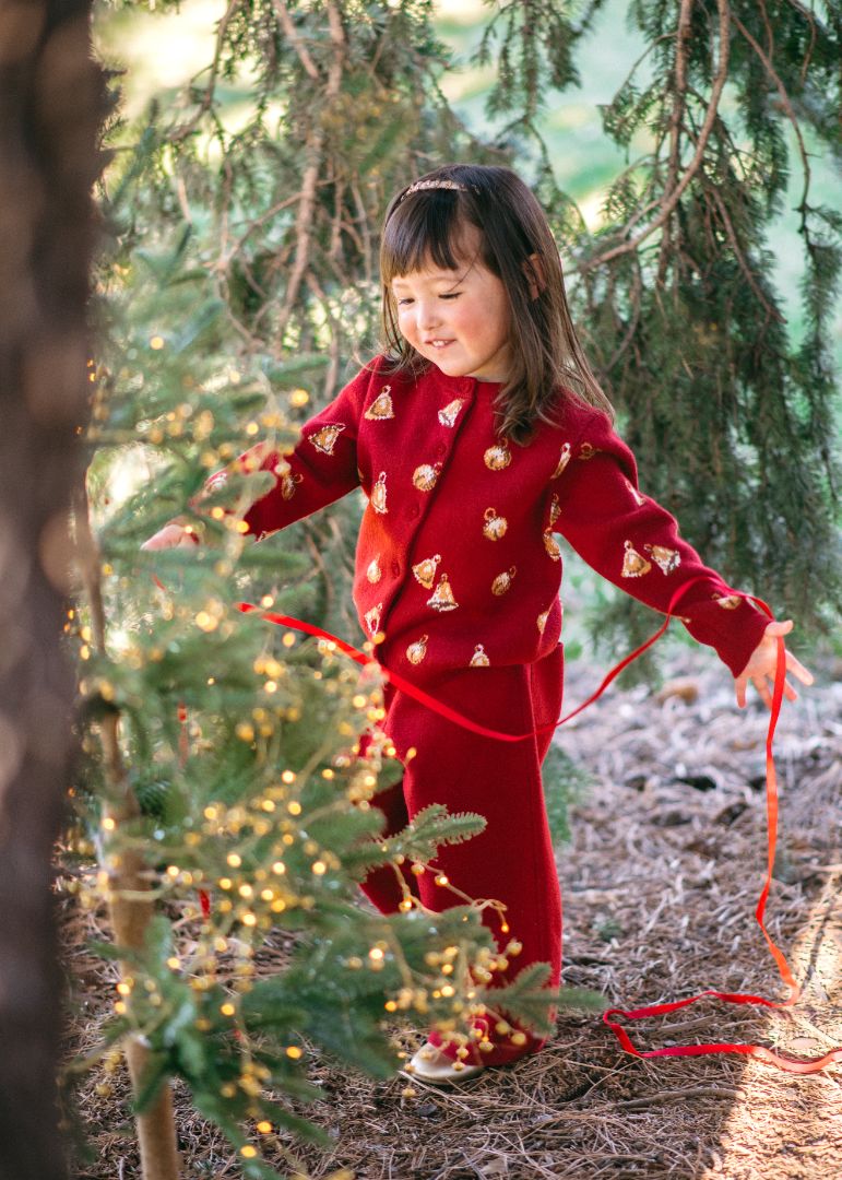 Girl decorating pine tree in Maroon Bells knit cardigan with vintage bell pattern and rich maroon base