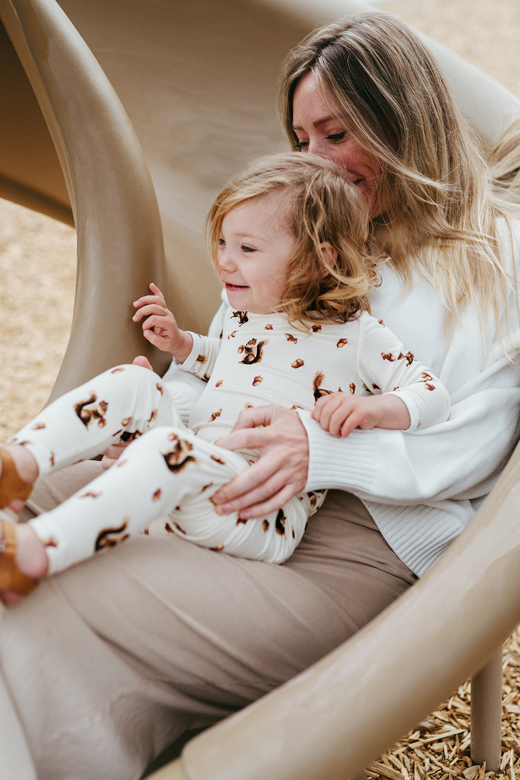 Mom holding child on playground slide, child wears Milkbarn's two piece pajama set in the chipmunk print