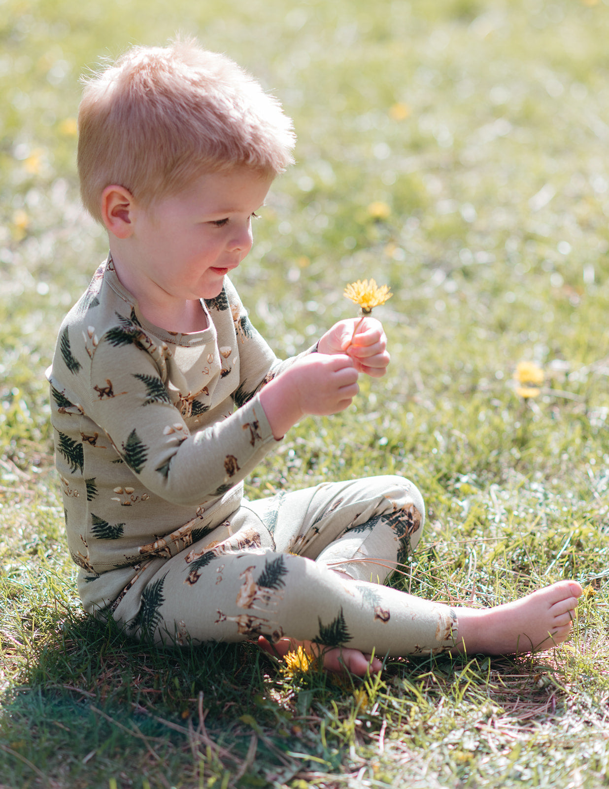 Little boy wearing Milkbarn's long sleeve two piece pajama set in the forest party print