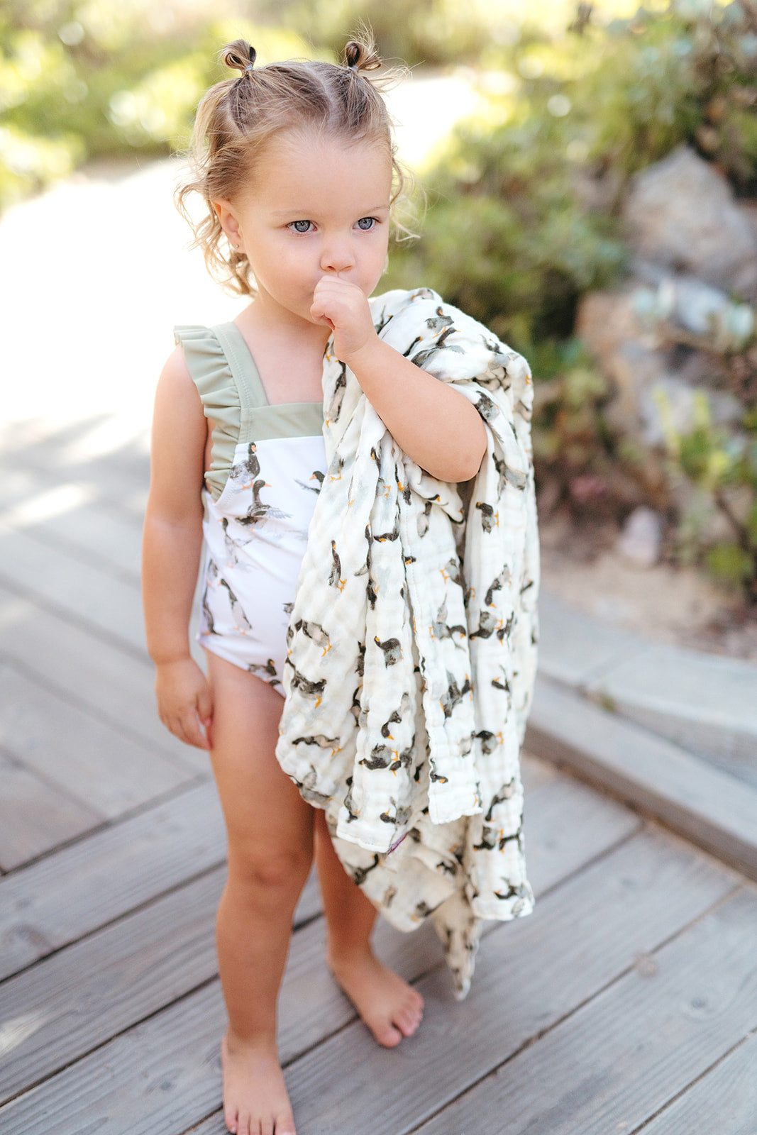 Young girl standing outdoors wearing Milkbarn Duck swimsuit and holding matching organic cotton towel, ready for the pool