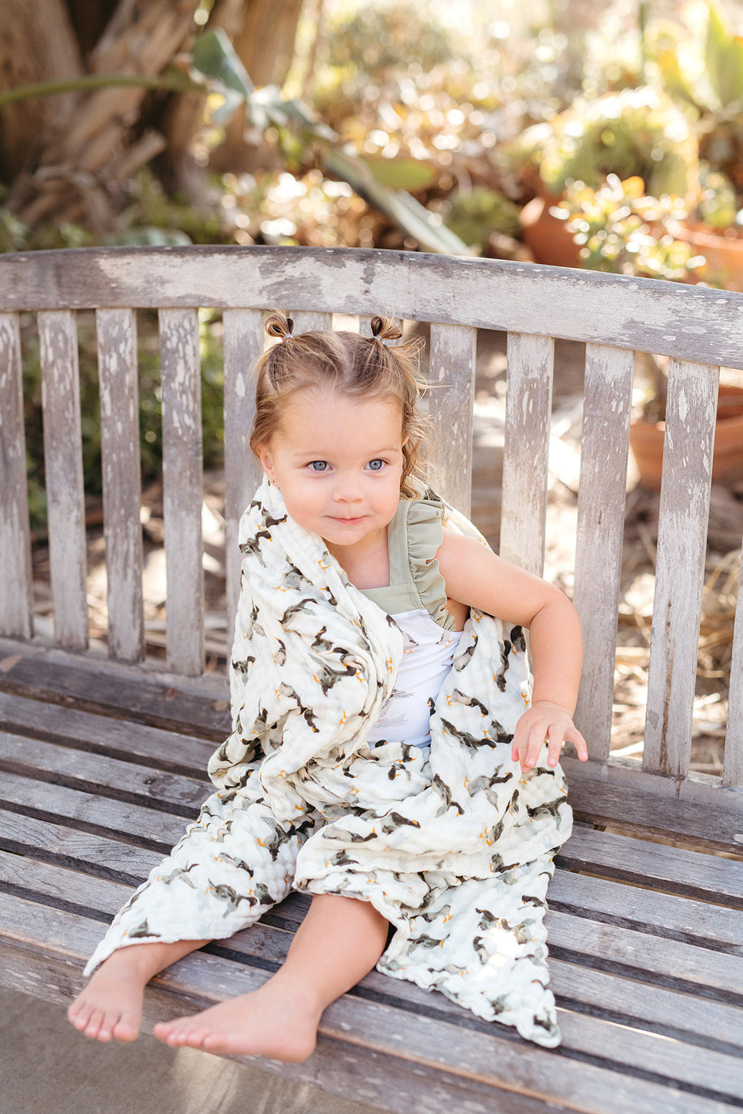 Little girl sitting on a wooden bench wrapped in Milkbarn Duck organic cotton towel, smiling after swim time, cozy and soft for kids.