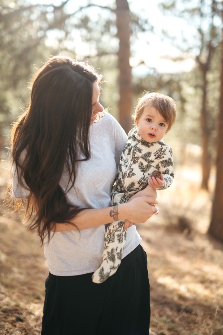 Baby boy in Pine print bamboo cotton zipper footie held by mom in forest during fall