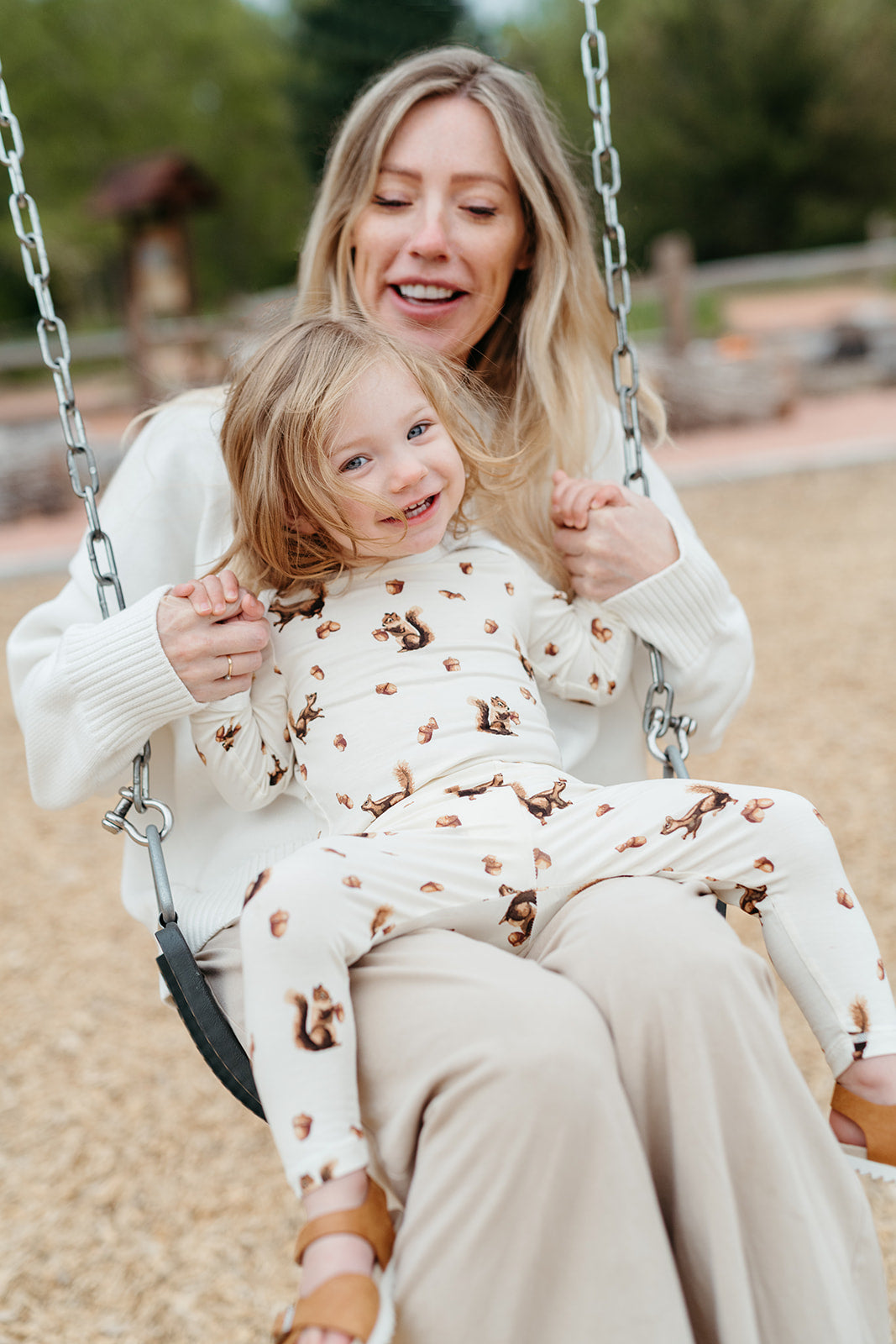 Mom and child on playground swings, child wears Milkbarn's pajama set in the squirrel print