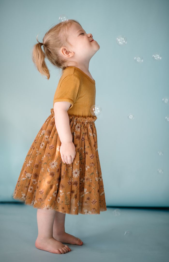 Toddler girl wearing Wildflower bamboo tulle ballet dress stands facing sideways surrounded by bubbles