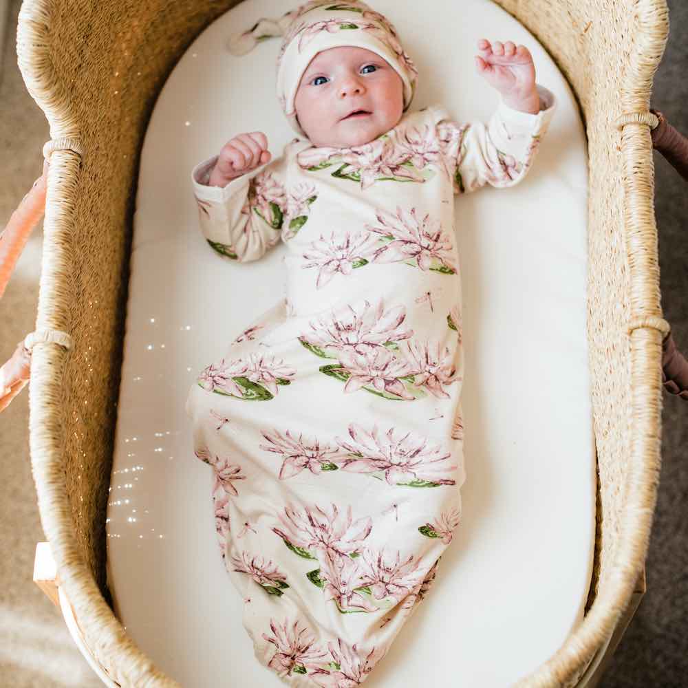 Little Newborn Baby in a Bassinet Wearing a Bamboo Gown and Hat Set in the Water Lily Print by Milkbarn Kids