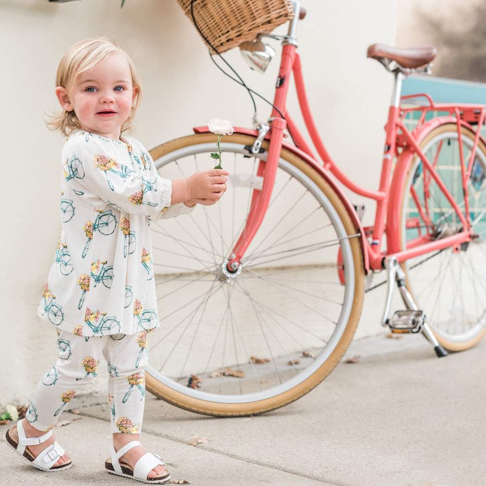 Baby girl next to a pink bicycle wearing Milkbarn Kids bamboo Dress and Legging Set in Bamboo Floral Bicycle Print