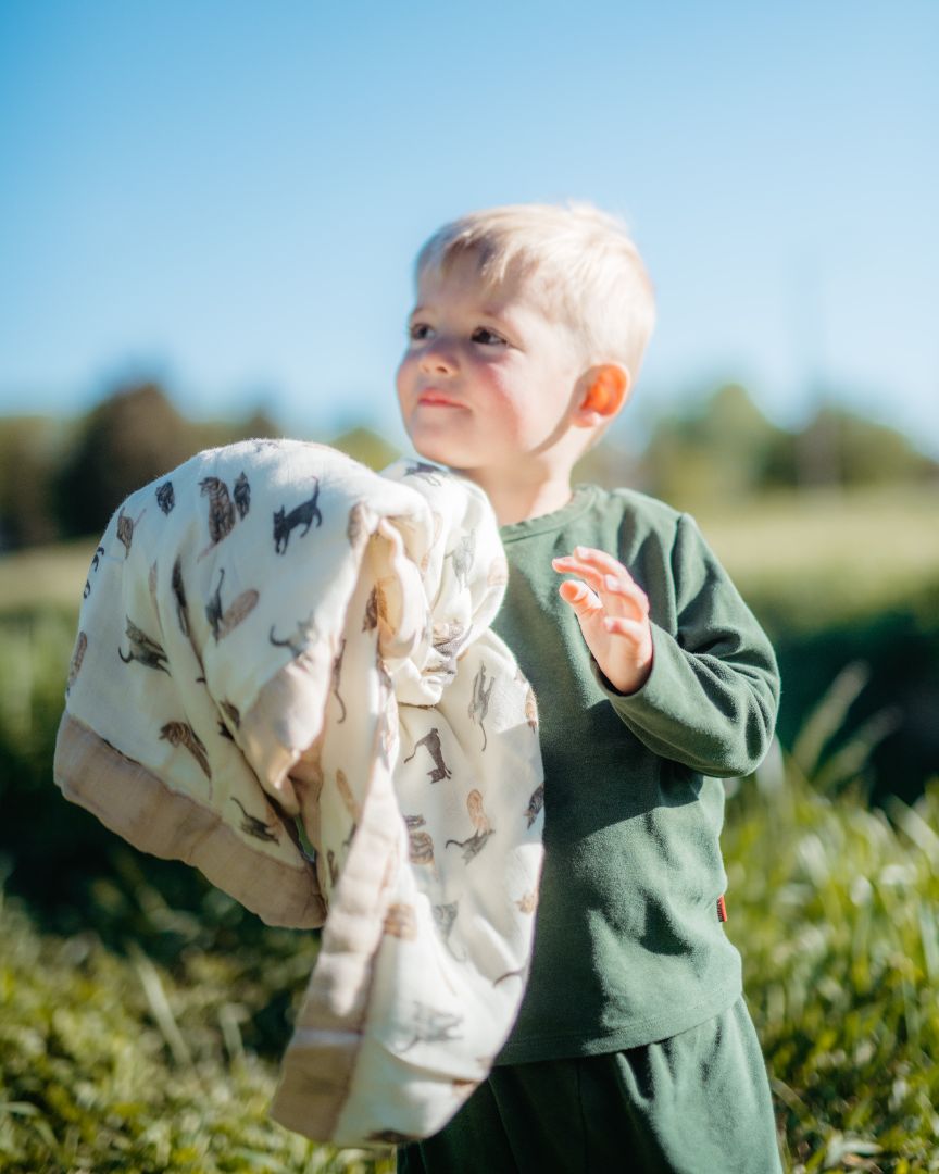 Young boy holding a folded Milkbarn Big Lovey blanket in Cat print made from soft bamboo-cotton blend.