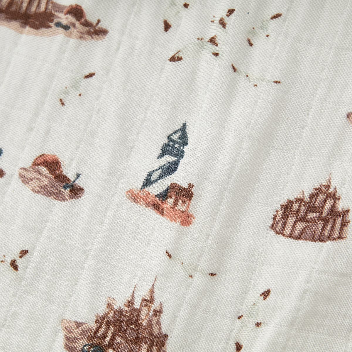 Closeup of Milkbarn Sandcastle Organic Cotton Muslin Swaddle Blanket, showing soft breathable 100% organic cotton with playful sandcastle, lighthouse, and seagull print for sensitive skin