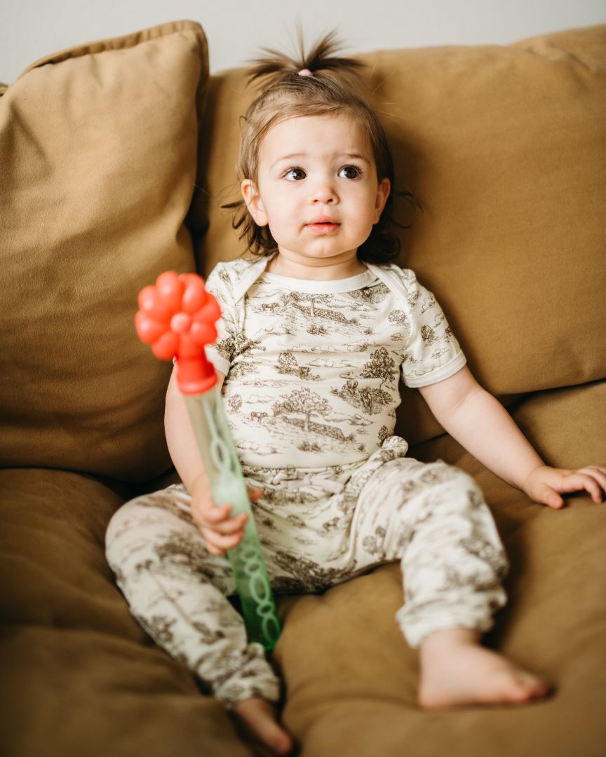 Child sitting on a couch wearing comfy jogger pants with an elastic waistband, drawstring, and pockets, styled with a Country Toile printed one piece.