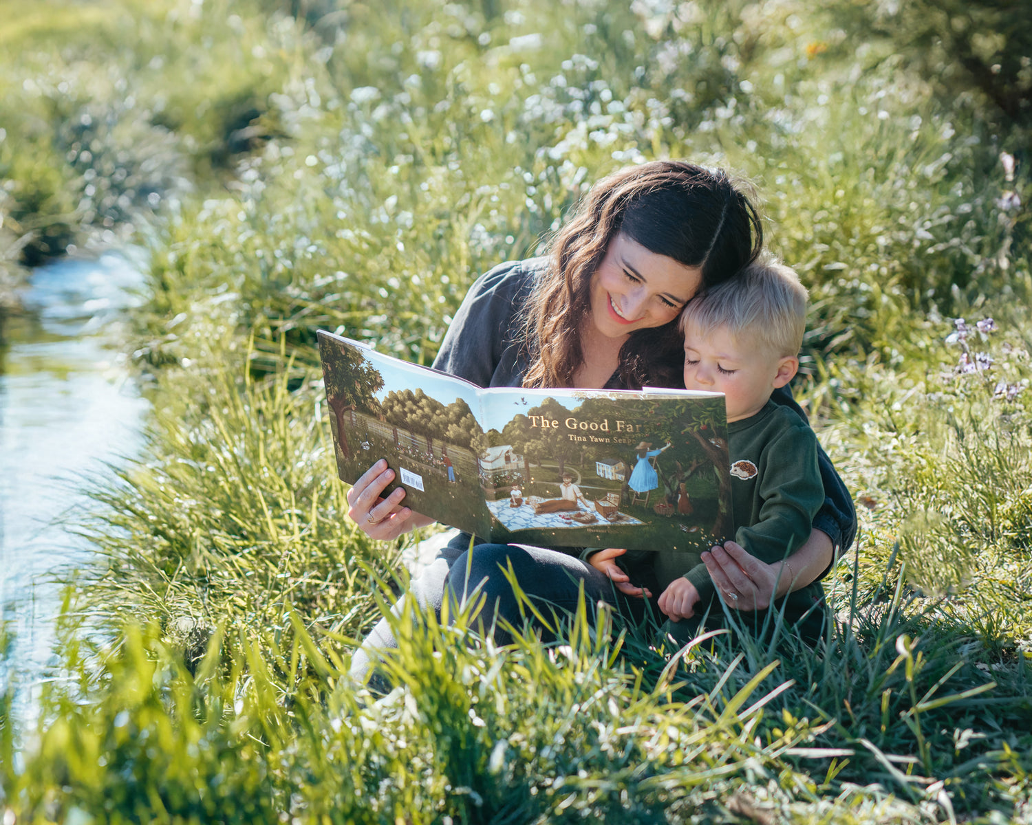 Mother reading The Good Farmer by Tina Yawn Seago to her child. This children’s book is for ages 3–6 celebrating love, kindness, and caring, featuring a gentle farmer on a farm in dark green and brown, perfect for reading with matching Milkbarn Apple Orchard pajamas