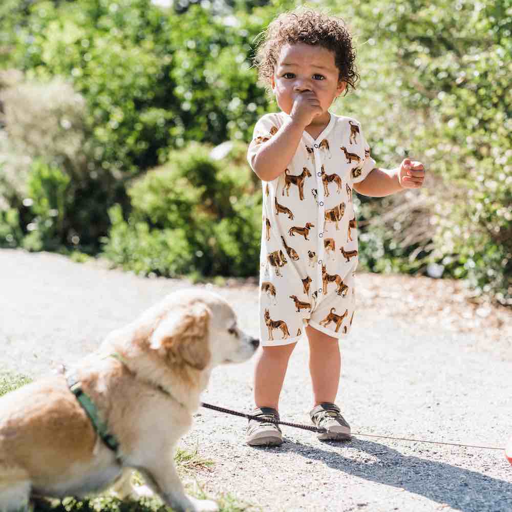 Dog and Little Baby Boy Wearing an Organic Cotton Shortall or Jumpsuit in the Natural Dog Print by Milkbarn Kids