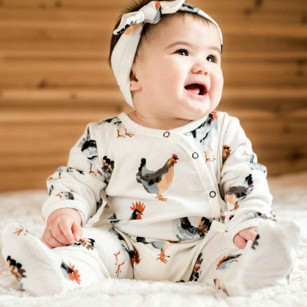 Little Baby Smiling in Milkbarn Kids Organic Cotton Footed Romper in the Chicken Print with Matching Headband