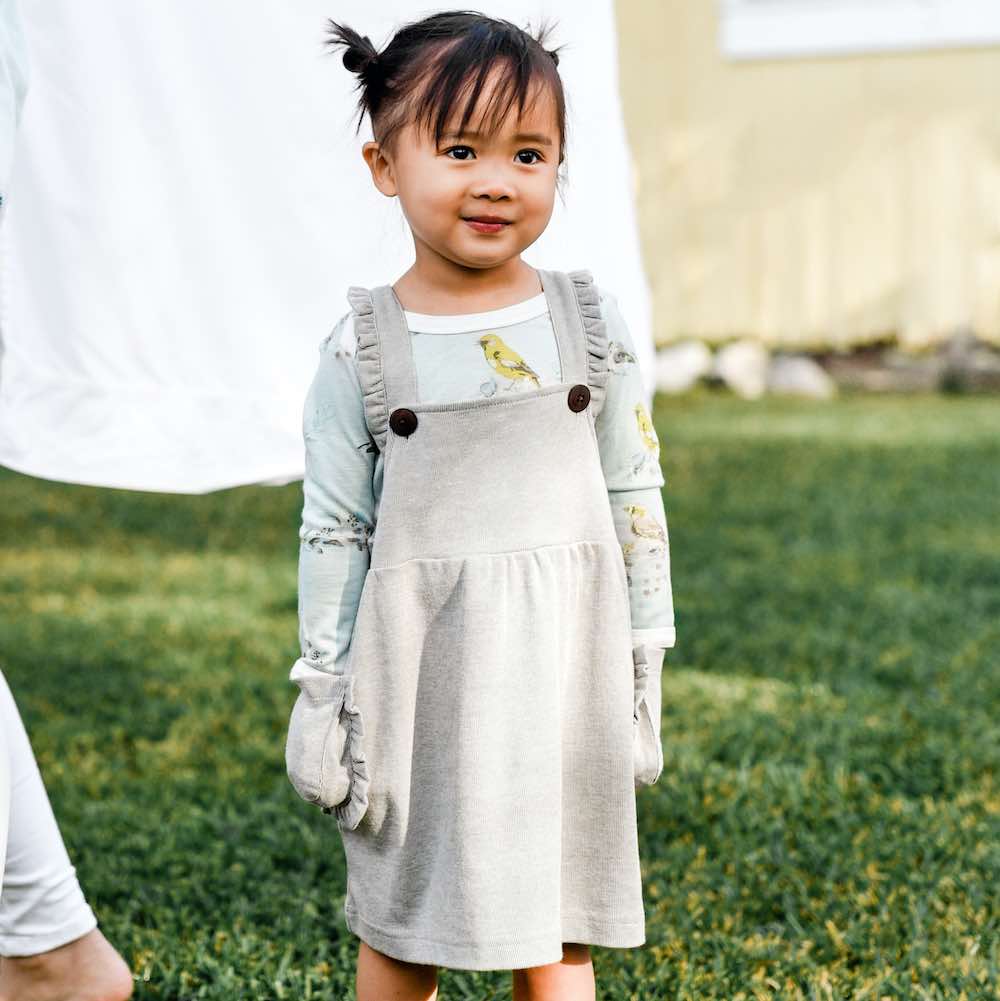 Little Baby Girl wearing a Dress Overall in the organic Cotton and Bamboo Grey Pinstripe Fabric by Milkbarn Kids