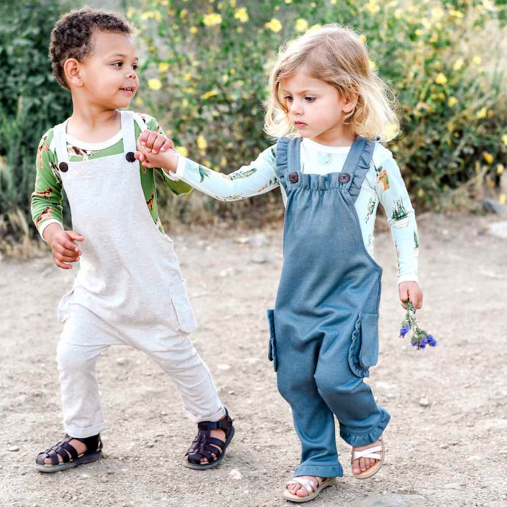 Little boy and girl wearing Milkbarn Kids Organic Baby Apparel in the Overall and Ruffle Overall in Denim and in Heathered Oatmeal