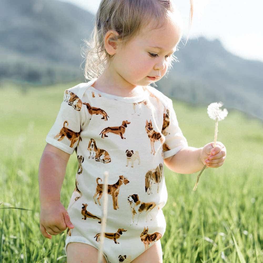 Baby Girl in a Grassy Field Wearing the Organic Cotton One Piece in the Natural Dog Print by Milkbarn Kids