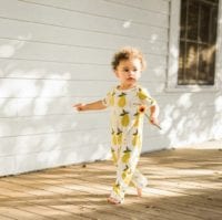Little Baby Walking on a Porch Holding a Flower Wearing the Organic Cotton Romper in the Per Print by Milkbarn Kids