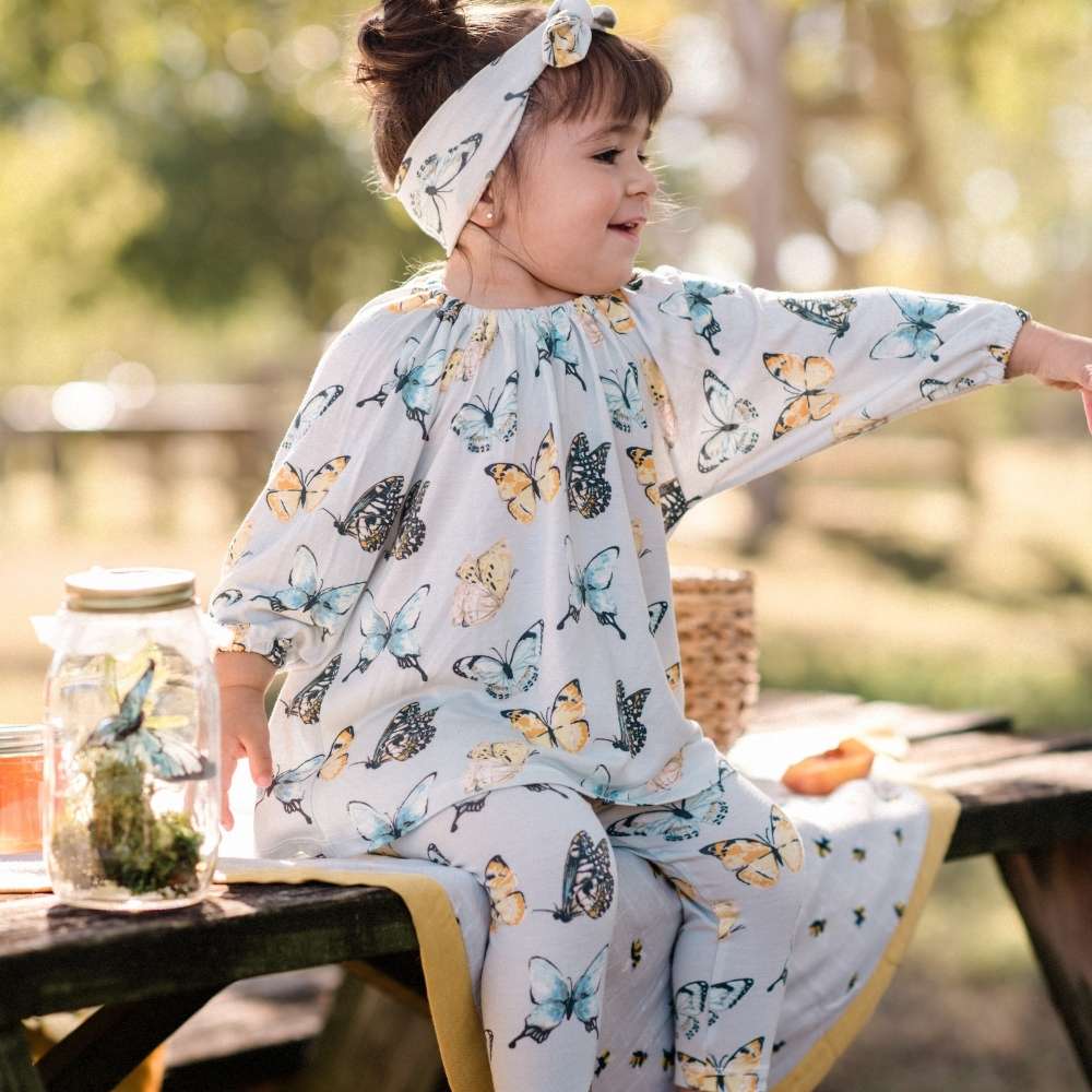 Baby Girl Sitting On A Picnic Table Wearing a Bamboo Butterfly Dress and Leggings by Milkbarn Kids
