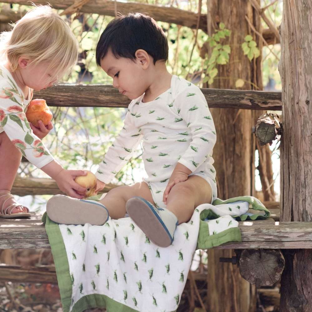 Two Babies on a Picnic Table Wearing the Grasshopper Organic Cotton Long Sleeve One Piece. Seen also is the Big Lovey Muslin Blanket in the Grasshopper print