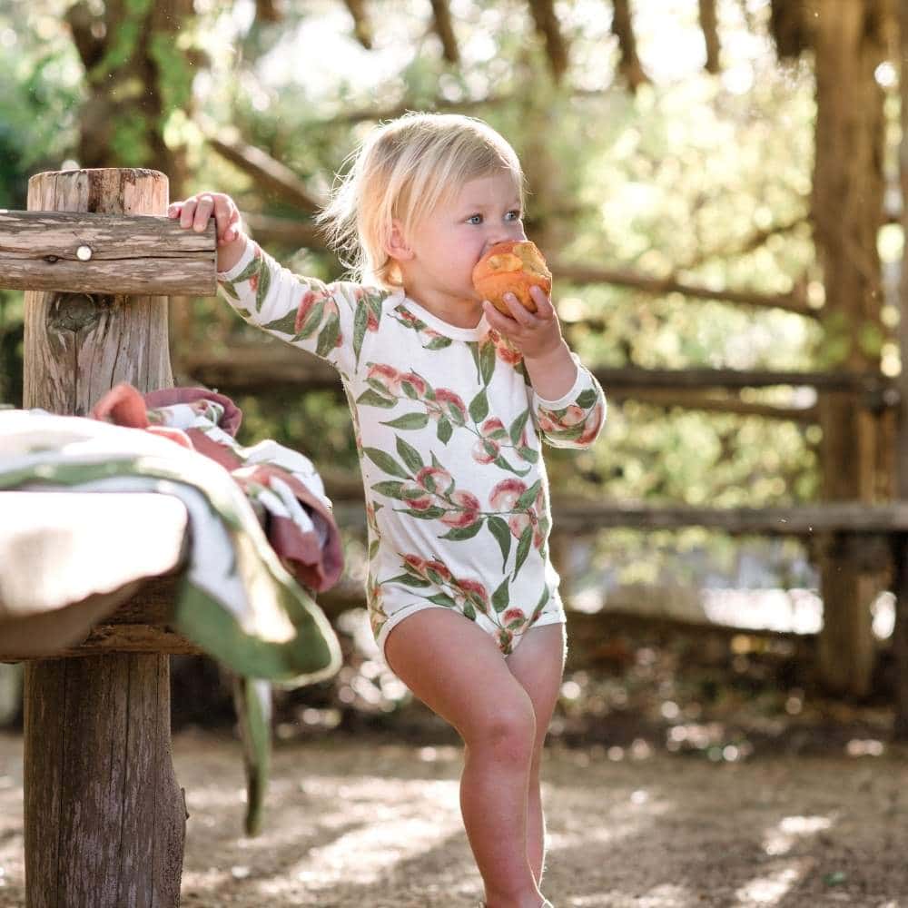 Little Baby Girl in a Park Wearing Peaches Organic Cotton Long Sleeve One Piece by Milkbarn Kids