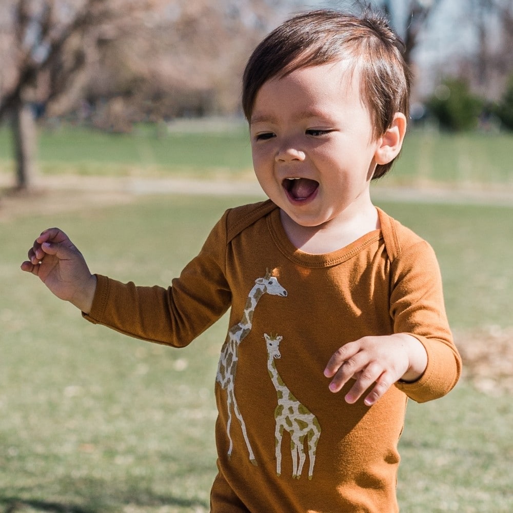 Baby boy running in a field wearing the Orange Giraffe Applique Organic Cotton Long Sleeve One Pice by Milkbarn Kids