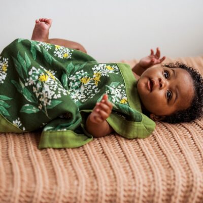 Baby girl lying on a bed covered with the Green Floral Mini Lovey Security Blanket by Milkbarn Kids