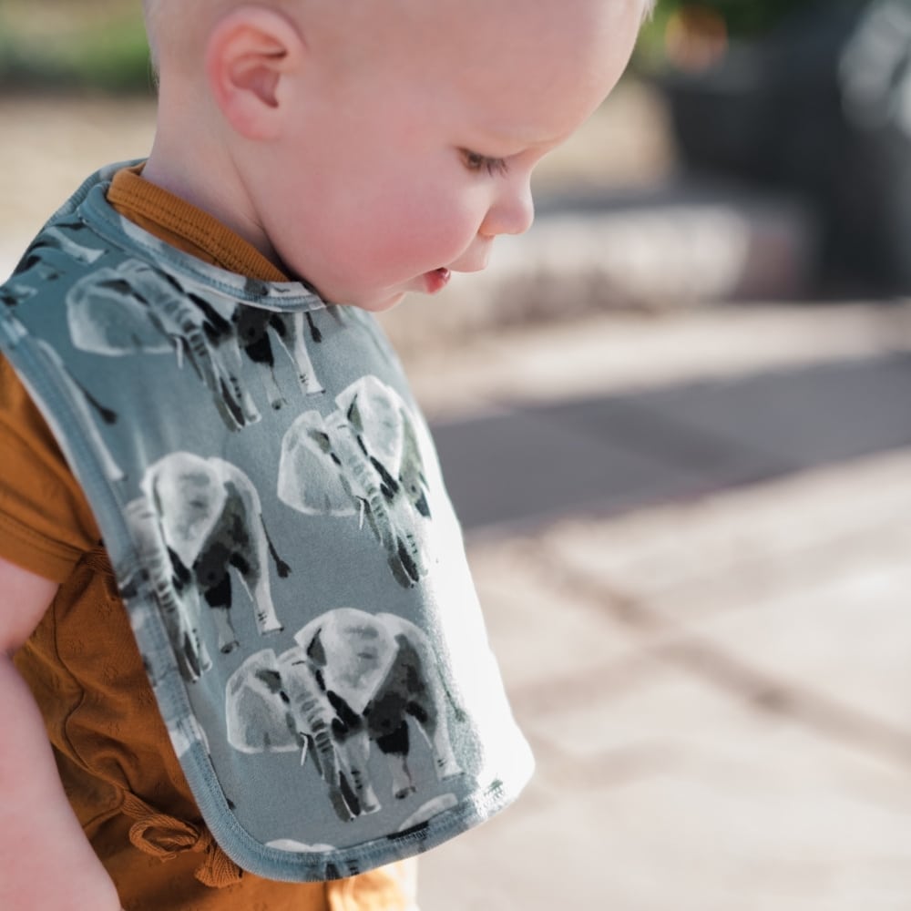 Baby Boy wearing an orange outfit outside with the Grey Elephant Organic Cotton Traditional Bib by Milkbarn Kids