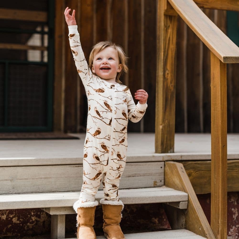 Little Boy on Cabin Steps Raising his Hand Wearing the Owl Bamboo Zipper Pajamas by Milkbarn Kids