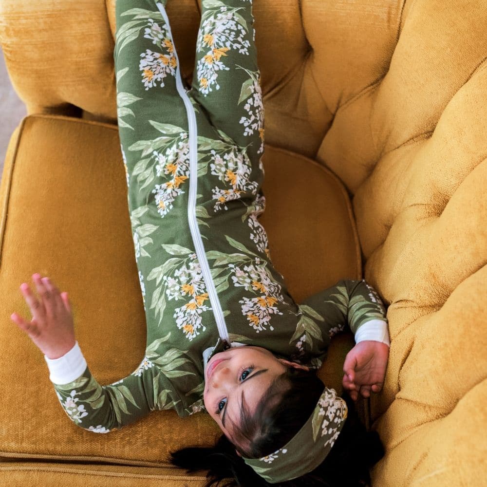 Little Girl Lounging on a couch wearing the Green Floral Bamboo Zipper Pajamas by Milkbarn Kids