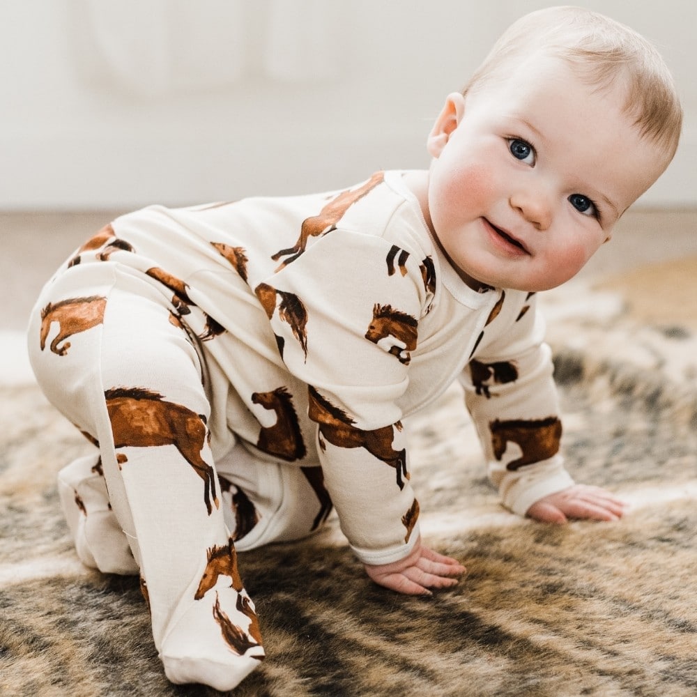 Baby crawling on a horse rug wearing Natural Horse Organic Cotton Zipper Footed Romper by Milkbarn Kids